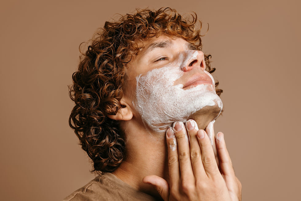 Handsome man enjoying beauty treatment while applying face cream and standing on brown bac