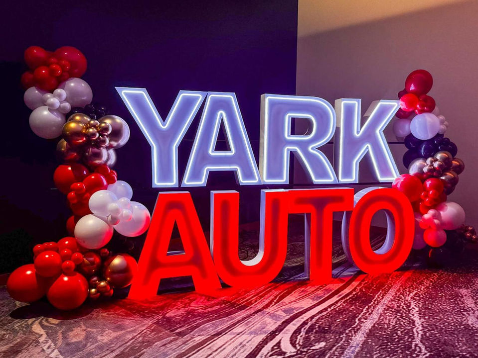 Illuminated YARK AUTO sign surrounded by red, white, and gold balloons.