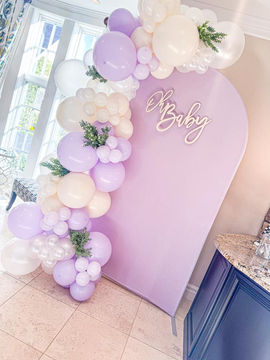 Light purple arched backdrop, 'Oh Baby' sign, lavender and white balloon garland.