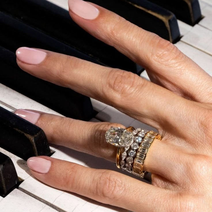 Manicured hand with pink nails and diamond rings resting on black-and-white piano keys.