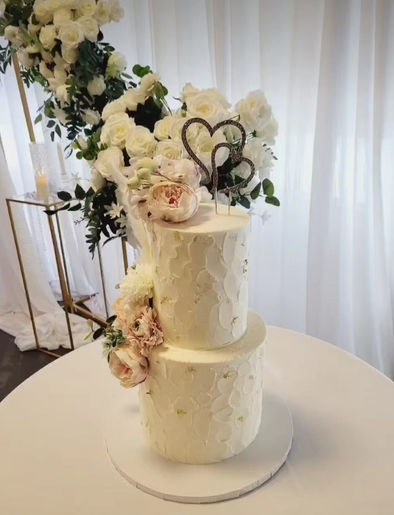 Custom white two-tier wedding cake decorated with roses and heart toppers.