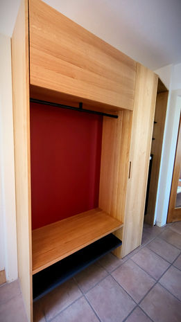 Massgefertigte Garderobe in Eiche massiv, natur geölt.
Schuhablage, Radiatorverkleidung und Tablare in Stahlblech/ Lochblech anthrazit beschichtet.

Die Garderobe bietet trotz den beengten Platzverhältnissen vom Eingangsbereich viel Stauraum. 

Der warme und natürliche Farbton vom Holz kombiniert mit der roten Rückwand strahlt Wärme aus und wirkt einladend. 