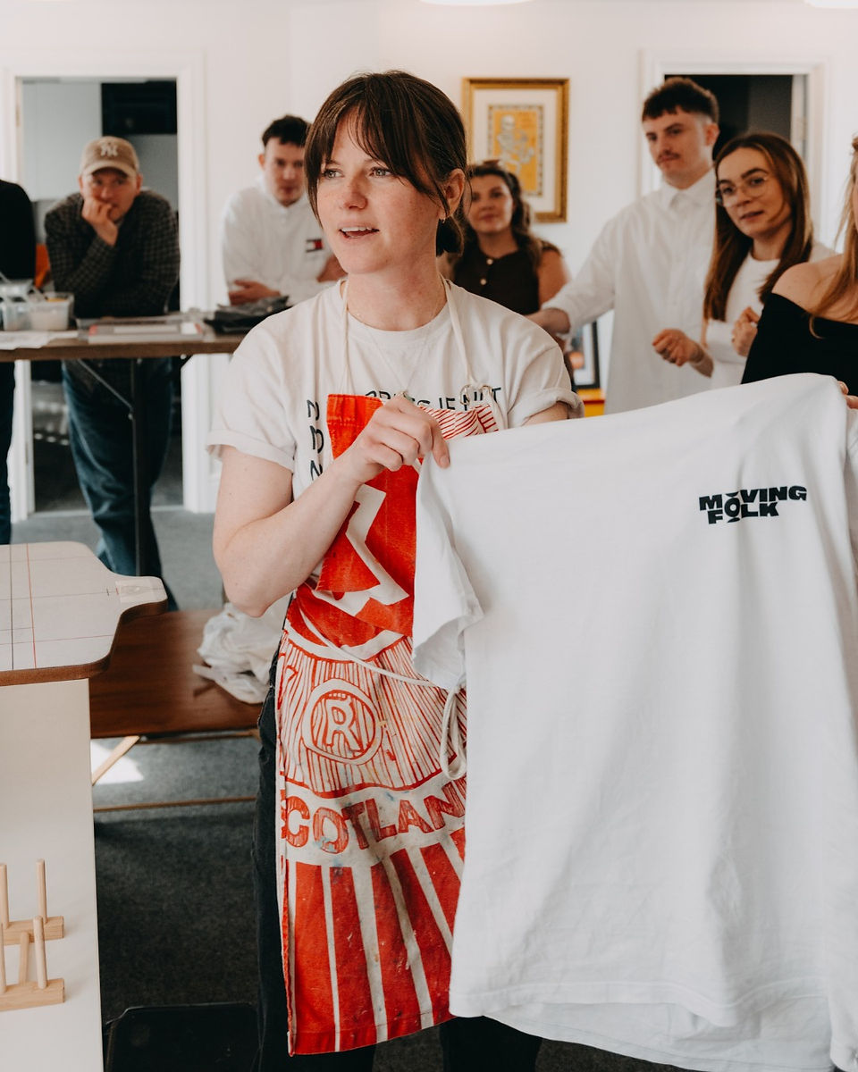 Laurie holding a freshly screen printed t-shirt with the Moving Folk logo on