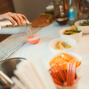 A bartender pouring a cocktail into a glass with bowls of garnishes at a birthday party