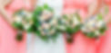 Bridesmaids holding floral bouquets in a row, wearing coral dresses at wedding.