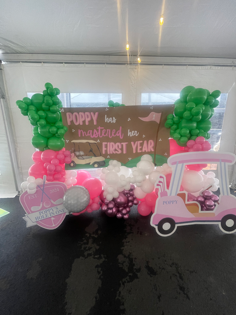 Poppy's first year celebration with golf cart and balloons, text reads: Poppy has mastered her first year