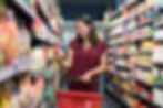 Woman at the grocery store holding a basket and reading nutrition label.