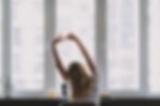 Waist up photo of young lady during a break sitting by the table and stretching her arms from hard work