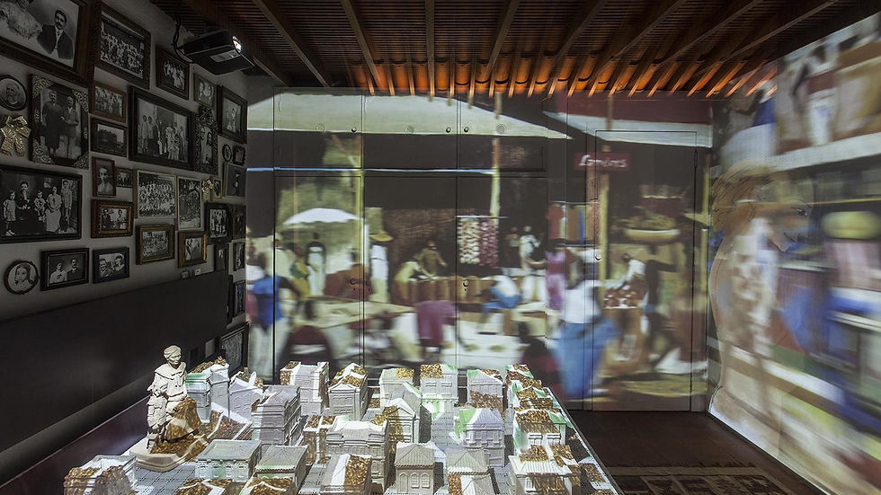Sala de exposição com parede de fotos preto e branco, maquete de cidade com projeção mapeada