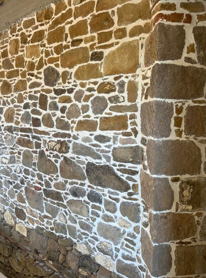 Close-up of a rustic, unevenly patterned dry stone wall with light-colored mortar joints on an active construction site.