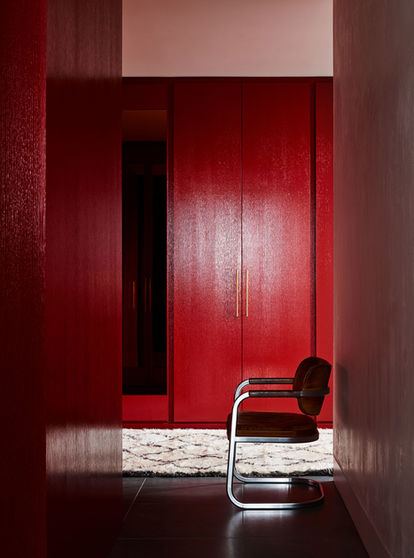 Looking into an intimate apartment foyer space with an electric red feature doorway wall and a simple black chair.