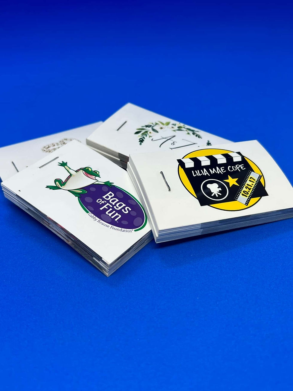Stacks of booklets on a blue surface display colorful logos: a frog with "Bags of Fun" and a film-themed design with text.