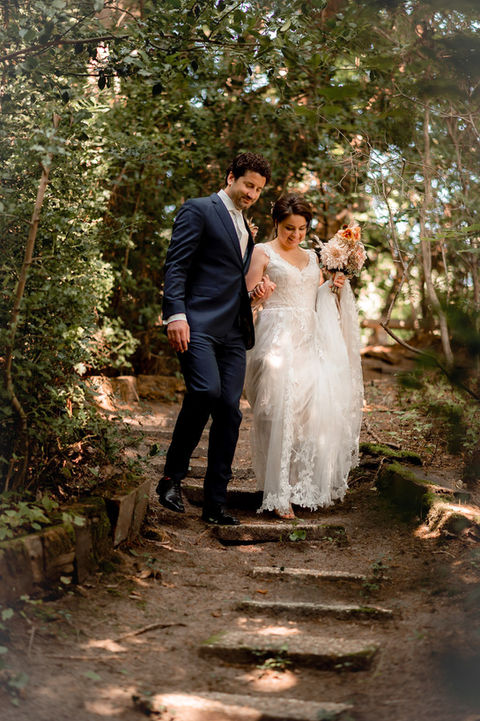 Stijlvol bruidspaar wandelt hand in hand over een bosrijk pad na hun exclusieve tuinhuwelijk in Wassenaar.