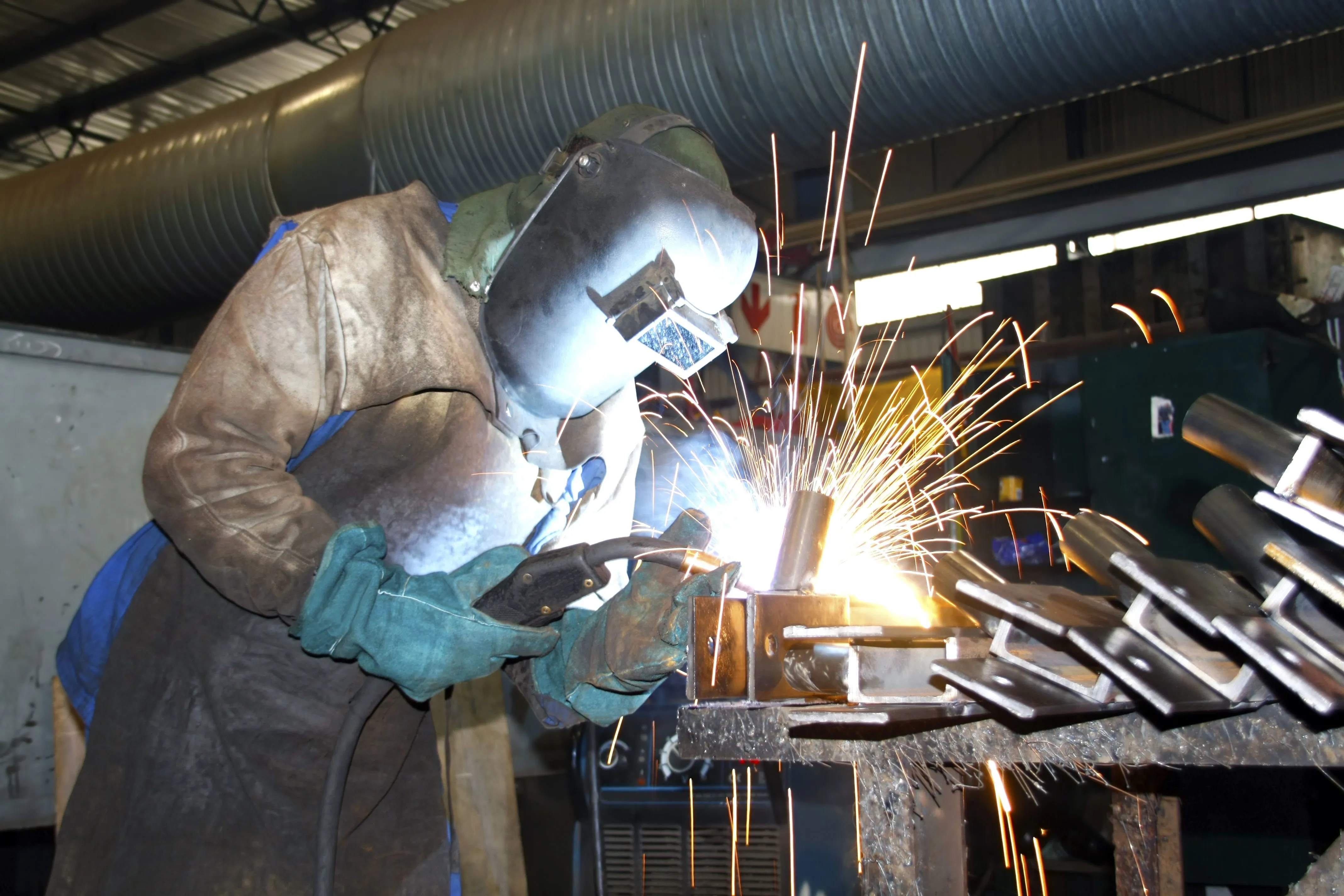 Welder working amid sparks in an industrial fabrication facility