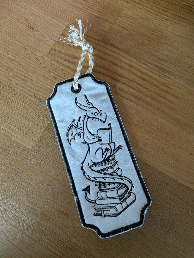 Handgemaakte bladwijzer met geborduurd draakje dat een boek leest, met koordje