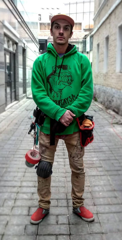 Iakov Kundin (Who Yasha Man) stands on a filming set with a variety of tools required for the set work, wearing green hoodie