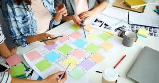 Personnes discutant autour d'une table avec des post-its colorés et des documents. Ambiance collaborative et studieuse. Fond de bureau.