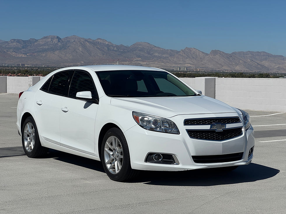 White sedan parked on a rooftop, with distant mountains under a clear blue sky. Chevrolet emblem visible on grille. economical, reliable, safe car