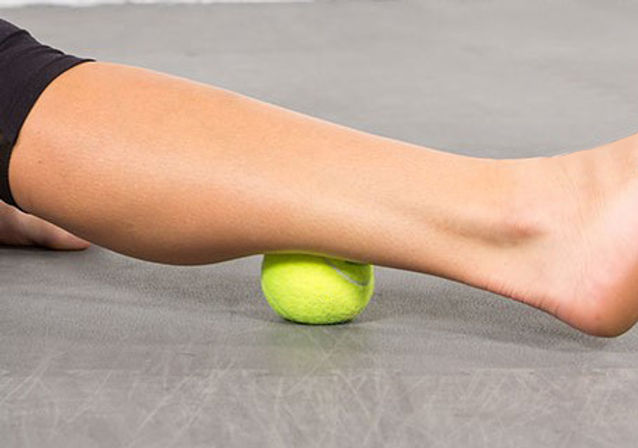 woman's calf massaging with tennis ball on the floor
