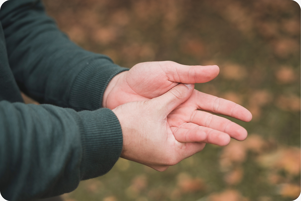 Hands in a green sleeve warming each other. Autumn leaves blur in the background, creating a cozy, outdoor vibe.