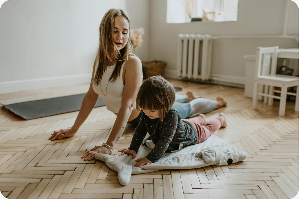 Woman and child doing yoga on wooden floor. The woman in white, the child in patterned clothes, both on mats, in a cozy, bright room.