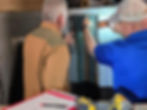 Two men inspect an HVAC system. One points, the other uses a tool. Notepad with diagrams in foreground, setting is industrial.