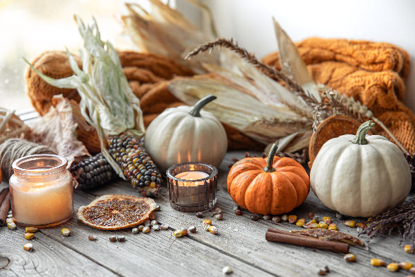 Composition automnale sur table en bois avec petites citrouilles orange et blanches, bougies allumées, épis de maïs colorés, bâtons de cannelle et écorces d’orange séchées – décoration chaleureuse pour célébrer Mabon.