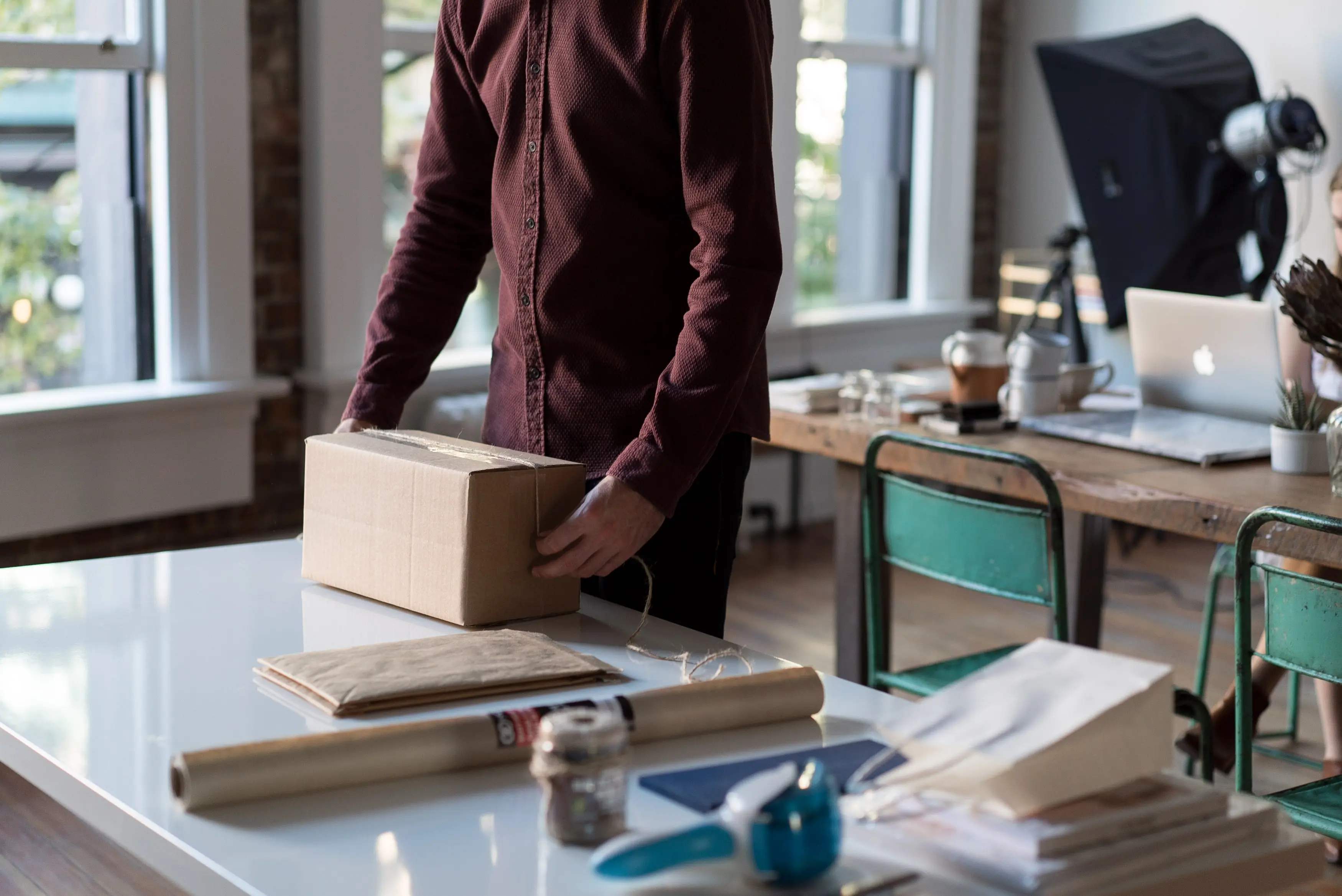 A man is holding a box in front of a desk.