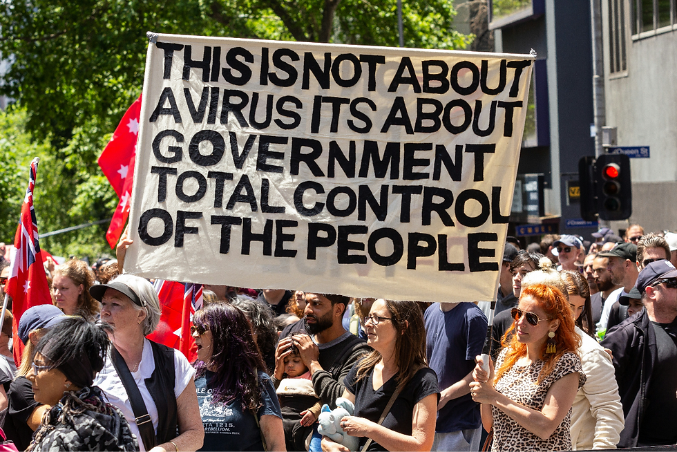 A white cloth sign held up at a protest, which reads: “This is not about a virus, it’s about government total control of people” in black capital letters.