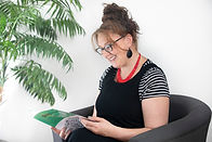 Karen Kyriakou is looking down at her book Strings Together reading it. She is relaxed and smiling. 