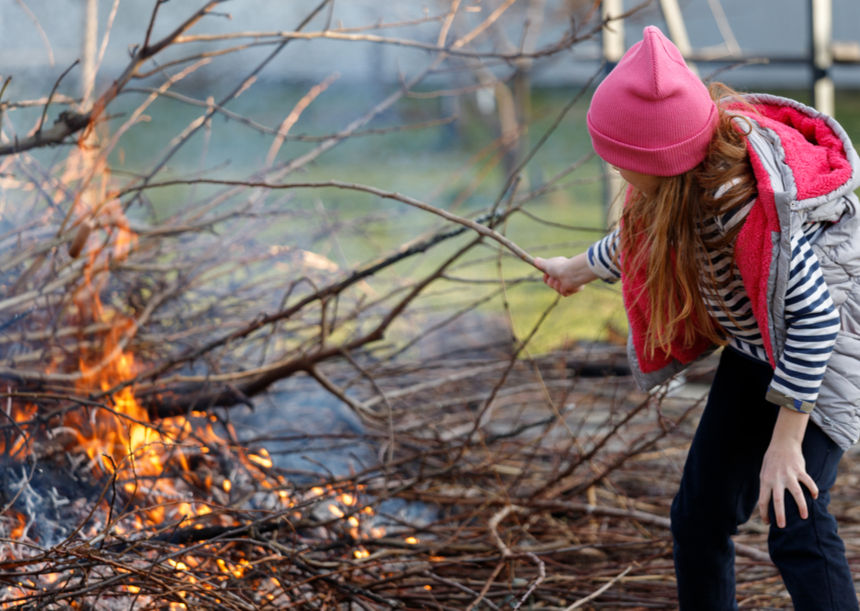 A girl in pink hat tending a bonfire outdoors.