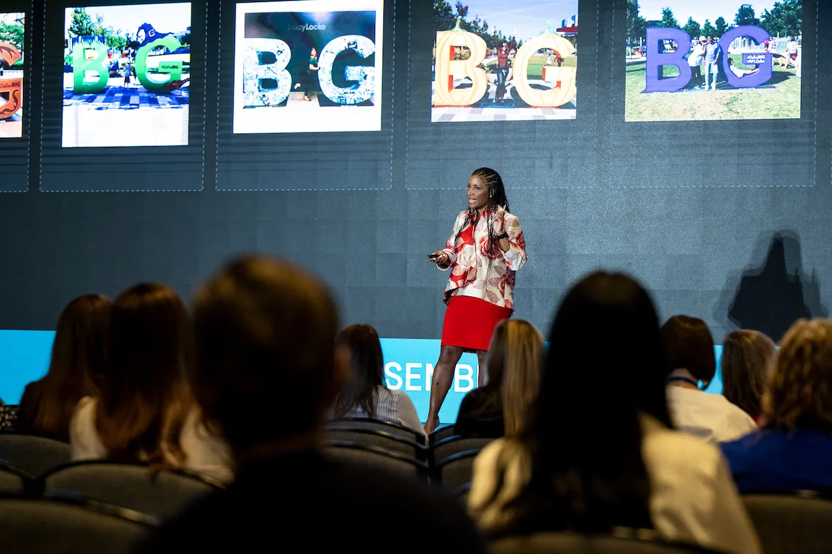 Noelle LeVeaux on stage with Dallas BIG campaign images on screen behind her