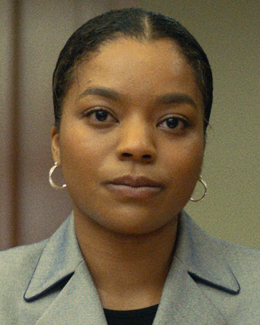 Baylee Berkley as Nia, seated at a courtroom table