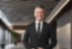 landscape_ image of a manned guard in a black suit and black tie smiling in a corporate bu