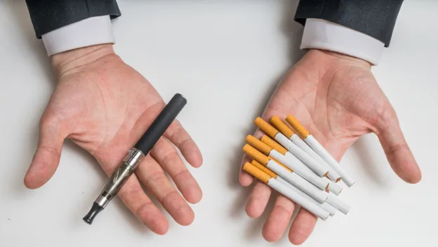 Imagen de dos manos abiertas, una sosteniendo un vaporizador y la otra cigarrillos.