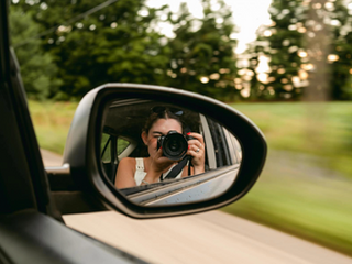 A reflection in a car mirror of a woman holding a camera