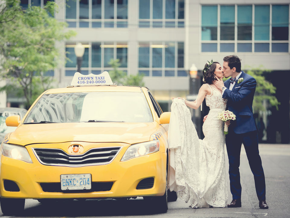 Urban wedding photo by top wedding photographers, Little Blue Lemon, of bride and groom kissing on the street next to a yellow taxi at the Rosewater Supper Club in downtown Toronto.
