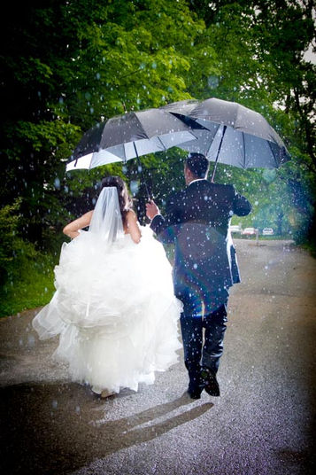 Bride and groom walking away down a park path holding umbrellas in the rain by Little Blue Lemon.