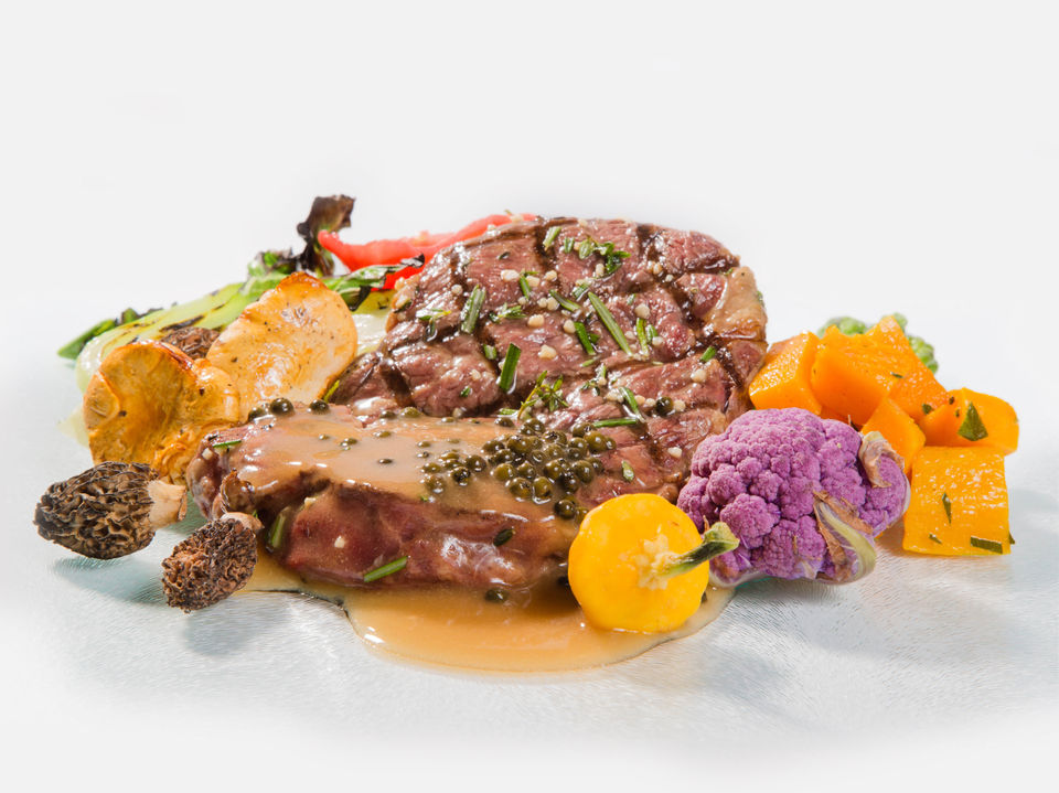 A New York Strip covered in peppercorn gravy and surrounded by ornate purple cauliflower and yellow tomato.