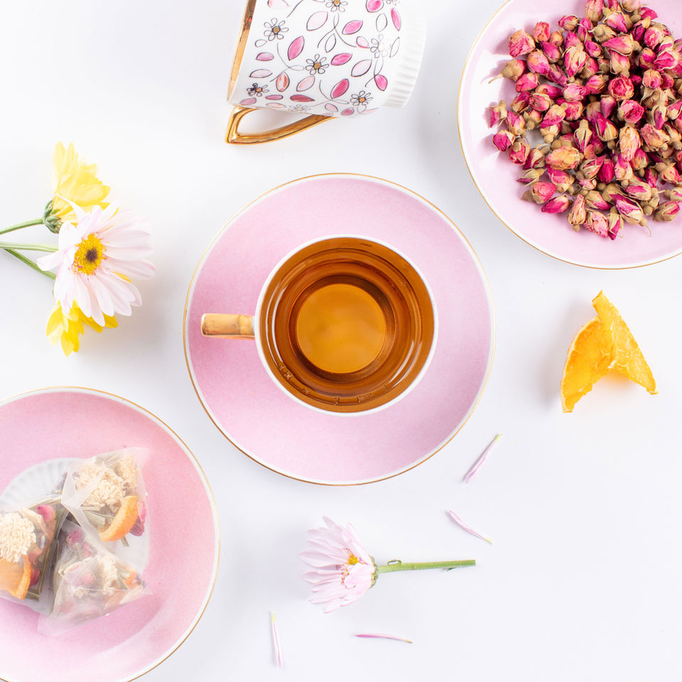 Rose hip tea presented in an antique pink and gold tea cup surrounded by loose rose hip flowers, and the handmade tea bag.