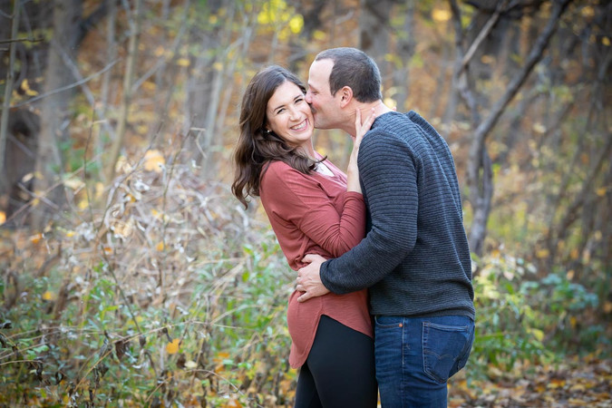 A man kisses his girlfriend on the cheek during their engagement shoot.