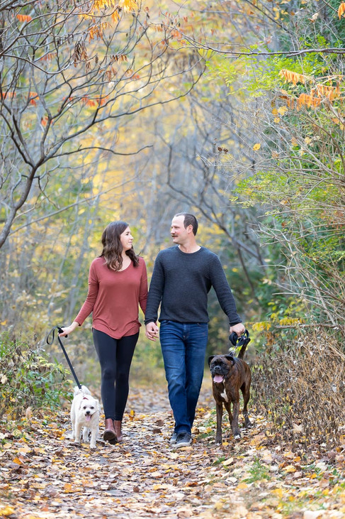 A newly engaged couple walk hand and hand looking at each other as they stroll through a forest path.