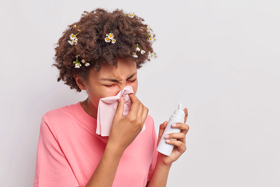Mulher com sinusite assoa o nariz e segura um aerossol para lavagem nasal