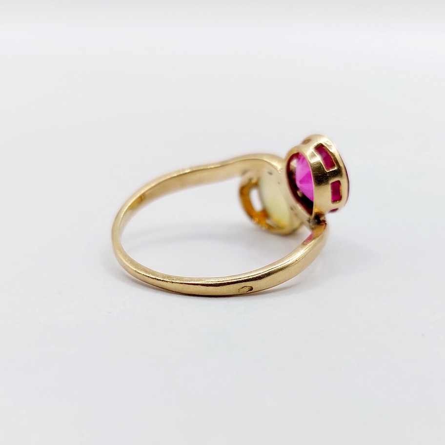 Bague en or rose avec une pierre rouge, vue de côté sur fond blanc.