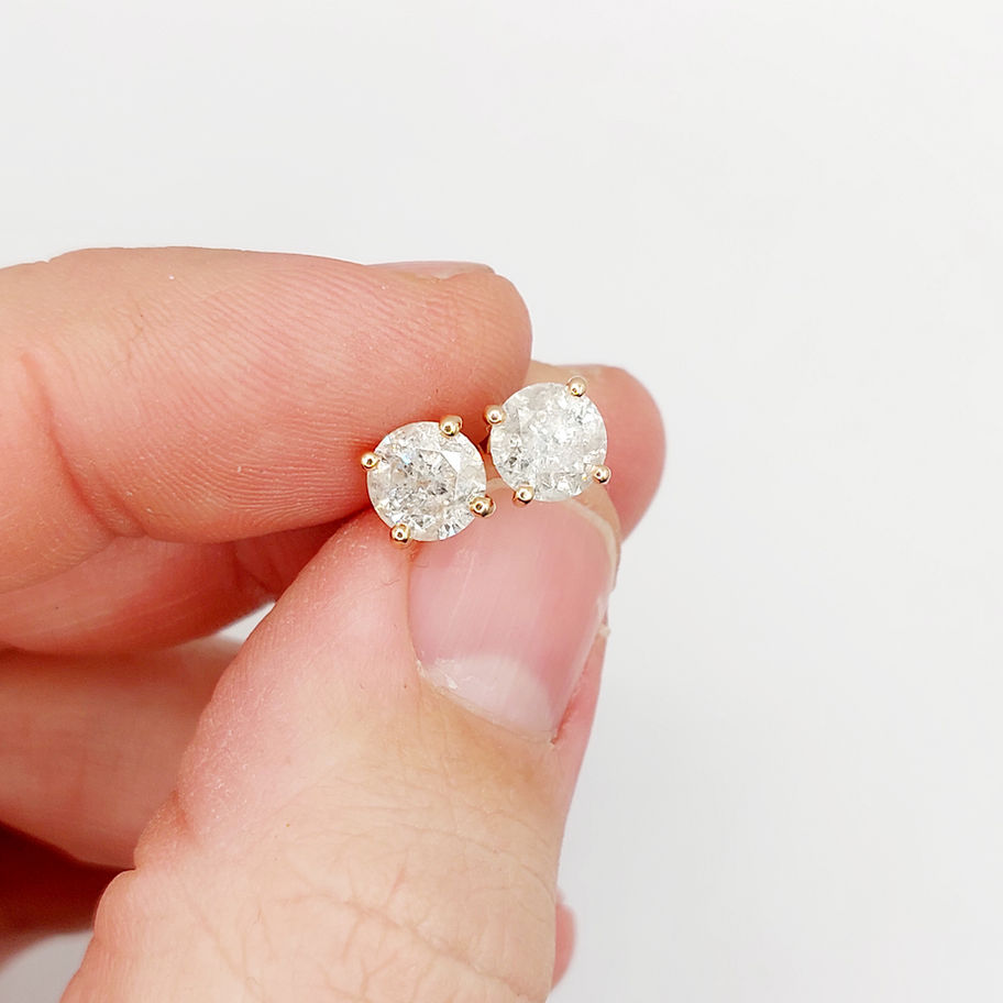 Main tenant, two diamond stud earrings held, white background, close up.