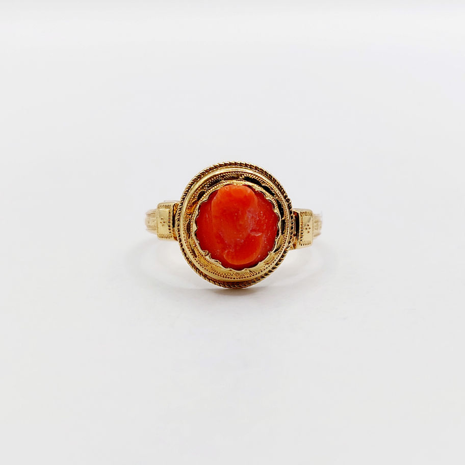 Bague en or avec un camée orange, sur fond blanc, bijou précieux.