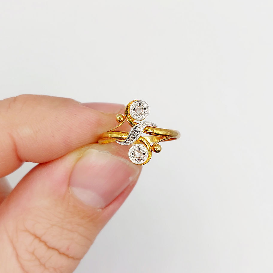 Bague en or avec diamants, tenue par une main sur fond blanc.