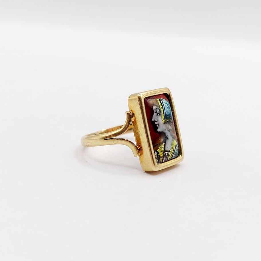 Bague en or avec un portrait féminin, détails et couleurs vives, sur fond blanc.
