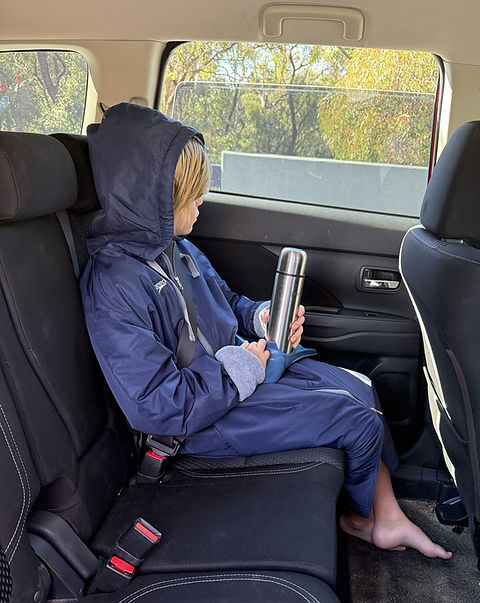 Child sitting in a car wearing a swim parka, holding a flask of hot chocolate, with swimming flippers on their lap
