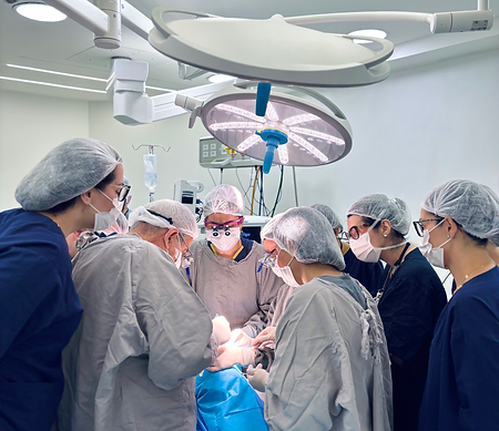 Alunos reunidos na sala de cirurgia ao redor da mesa cirúrgica, acompanhando cirurgias de estrabismo ajustável ao vivo.